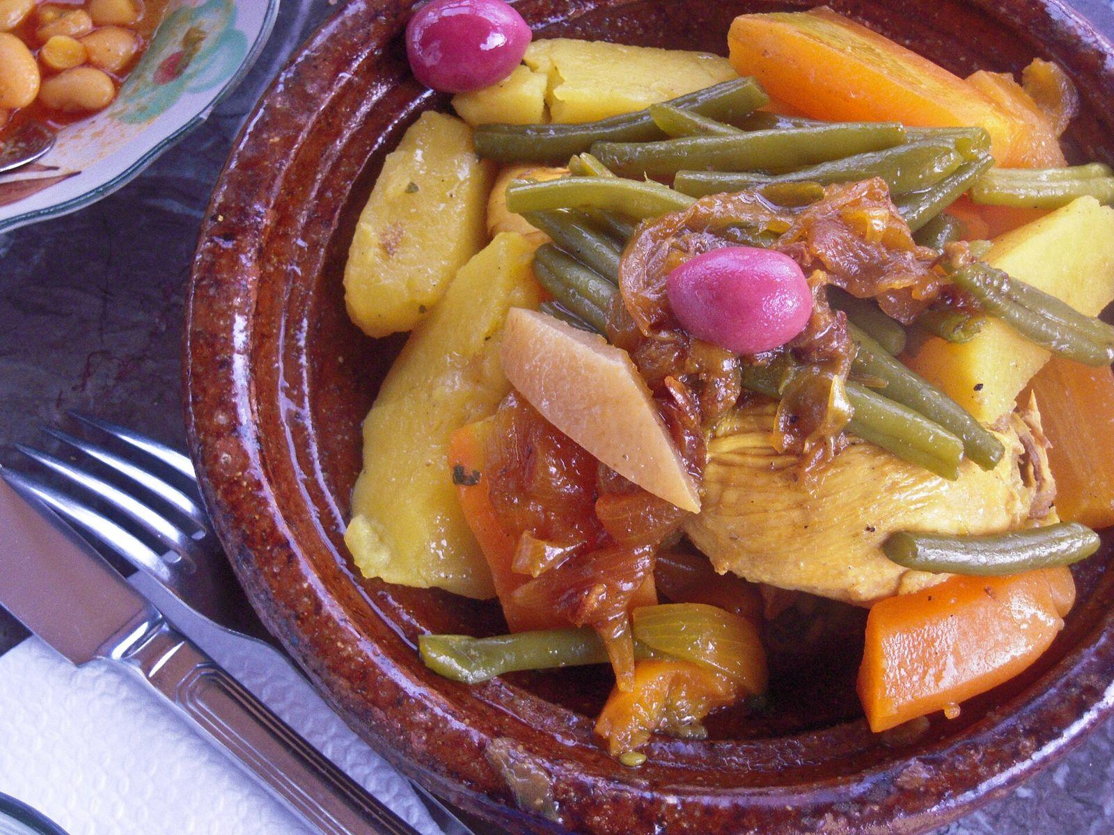 Chicken tagine with potatoes, carrots, green beans and red olives in a glazed clay dish