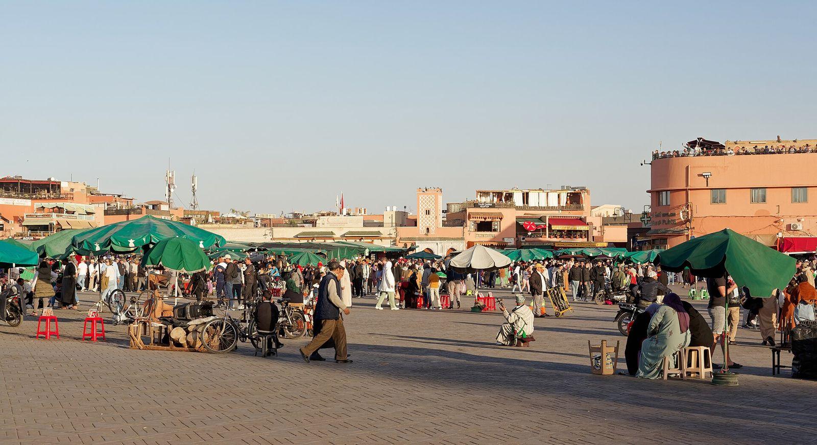 Jemaa el-Fna square on a sunny afternoon with green parasols, stalls, crowds and ochre buildings