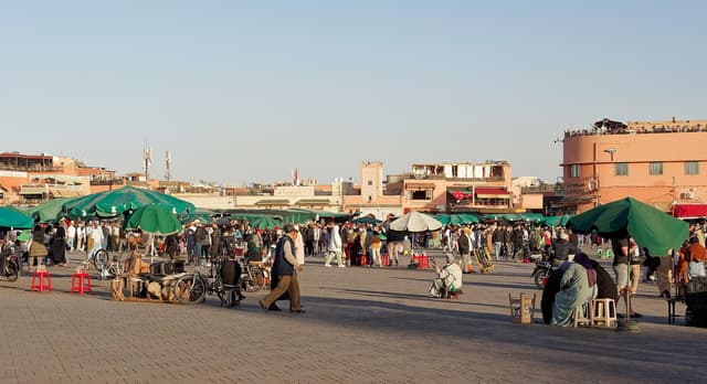 Jemaa el-Fna square on a sunny afternoon with green parasols, stalls, crowds and ochre buildings