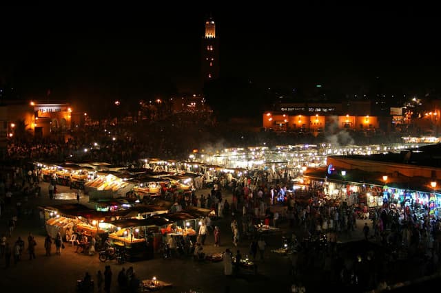 Jemaa el-Fna square at night with glowing food stalls, crowds and the lit Koutoubia minaret behind